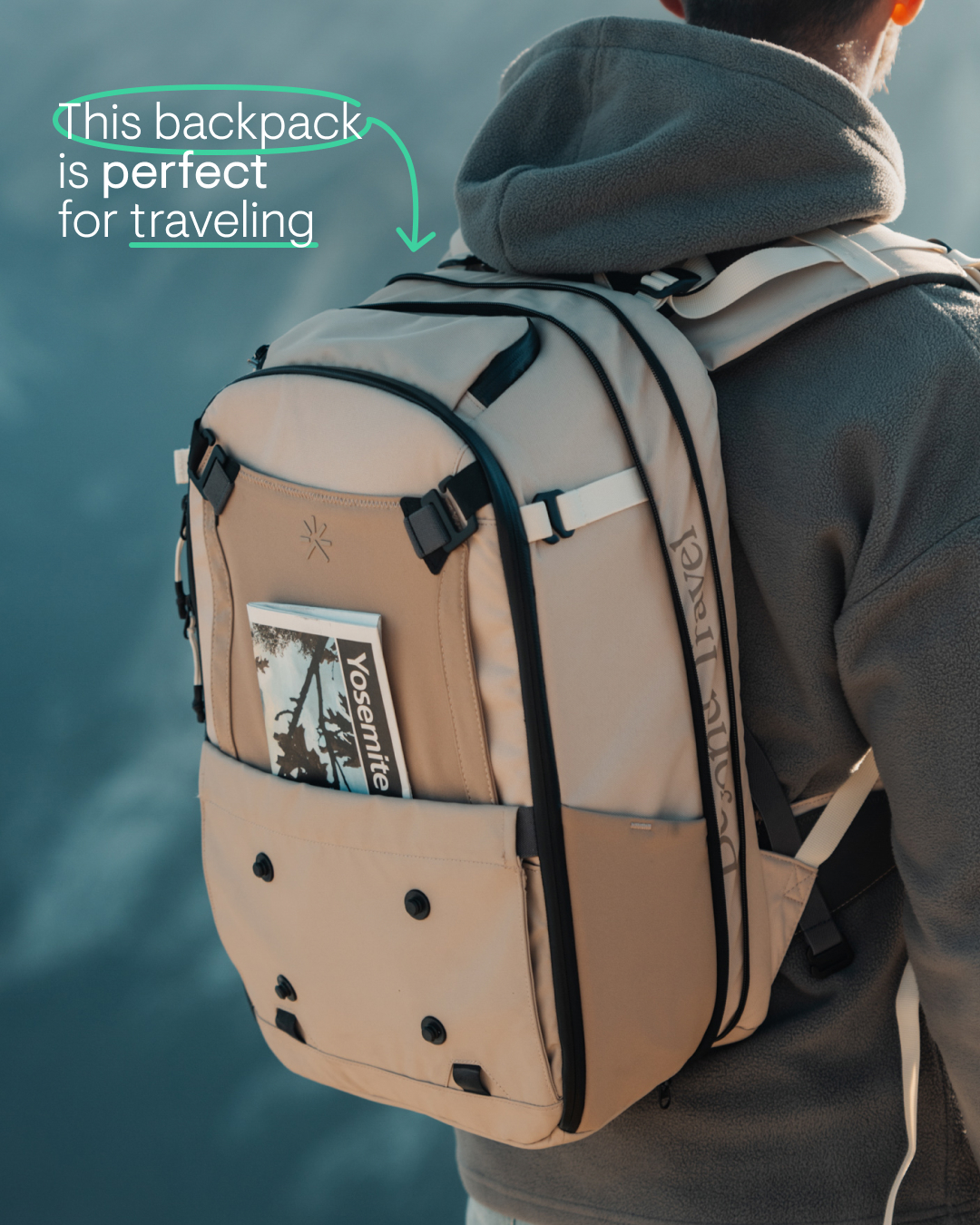 A person is shown from behind, wearing a large, beige backpack. The backpack has black zippers and straps, and a magazine with the word "Yosemite" is tucked into a front pocket. Green text with a curved arrow overlay reads, "This backpack is perfect for traveling." The background is a blurry, overcast sky.