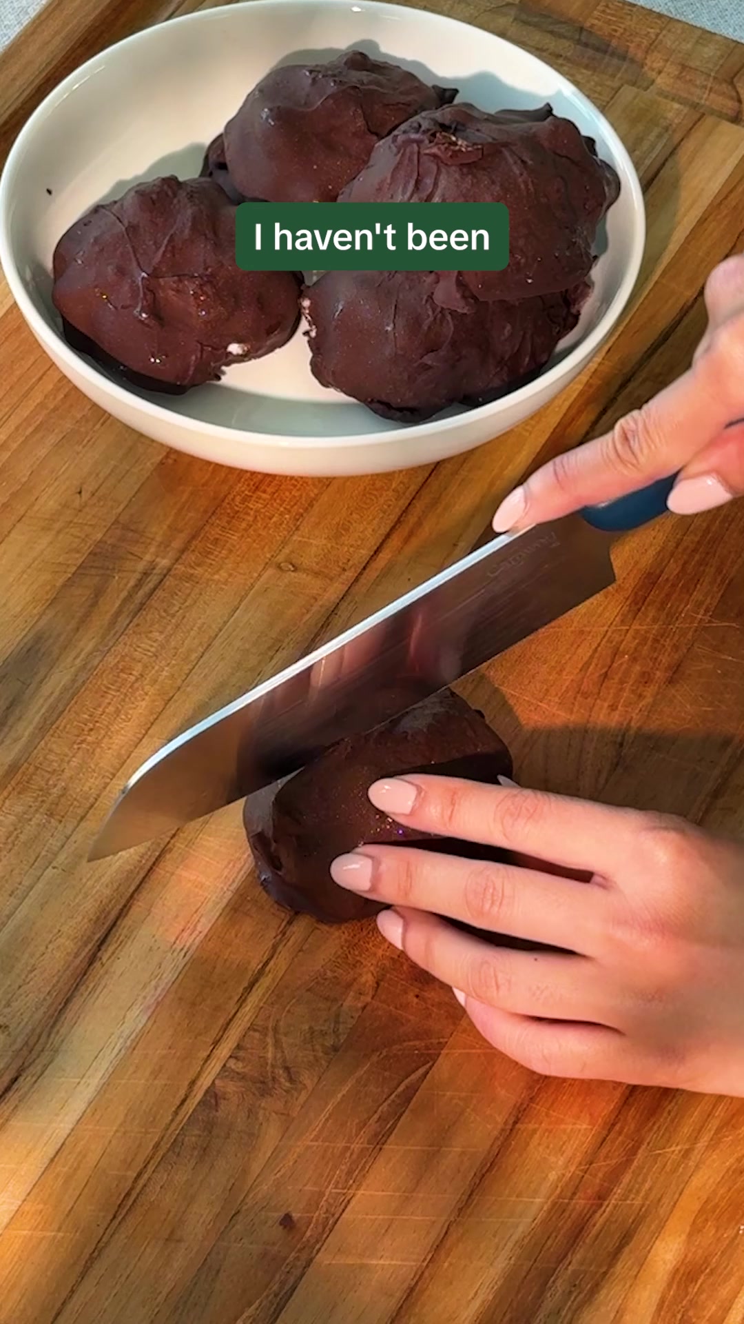 A white bowl filled with chocolate-covered desserts sits on a wooden cutting board. A person's hands are visible, holding a knife and cutting into one of the desserts. Green text overlay on the bowl reads "I haven't been". The ad copy features a question about Hungryroot and includes several positive customer reviews.