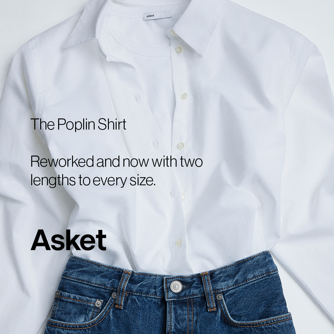 A close-up, top-down studio shot of a white button-down shirt layered over a white t-shirt, with the top portion of blue denim jeans visible at the bottom. White text overlays the shirt, reading "The Poplin Shirt" in a large serif font, followed by "Reworked and now with two lengths to every size." in a smaller, lighter font. The brand name "Asket" is displayed prominently in a bold, black sans-serif font at the bottom left of the shirt. The overall aesthetic is clean, minimalist, and focused on the product details.