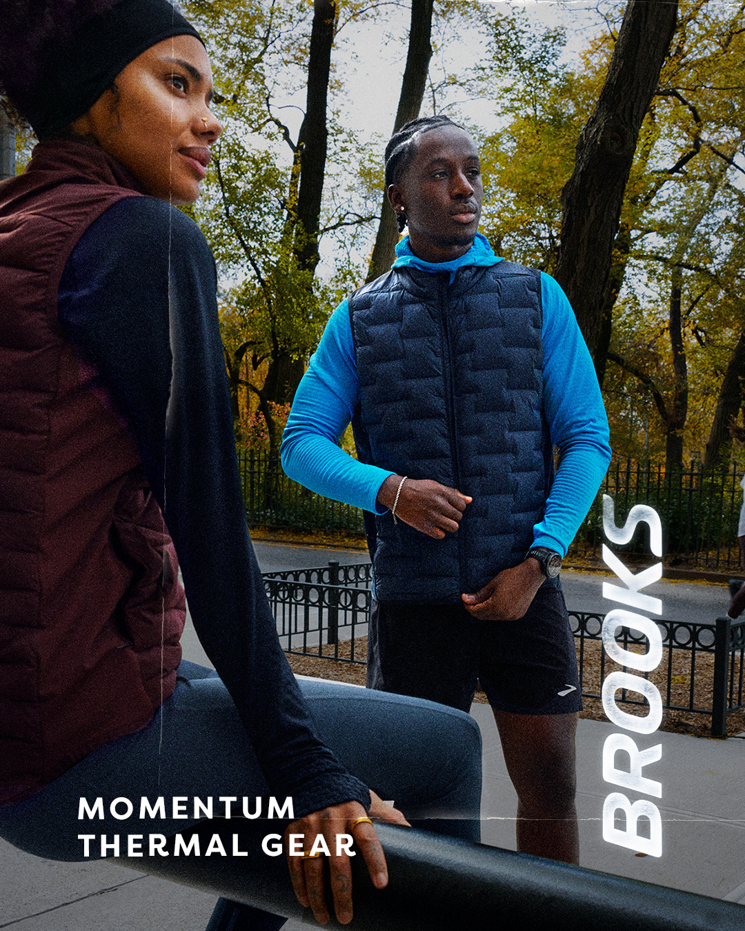 Two people are shown outdoors in a park setting with trees in the background. The person on the left is wearing a maroon vest over a dark long-sleeved shirt and dark pants. The person on the right is wearing a blue long-sleeved shirt under a dark puffer vest and black shorts. The text "MOMENTUM THERMAL GEAR" is displayed in large white font on the left side of the image. The brand name "BROOKS" is written vertically in large white font on the right side of the image.