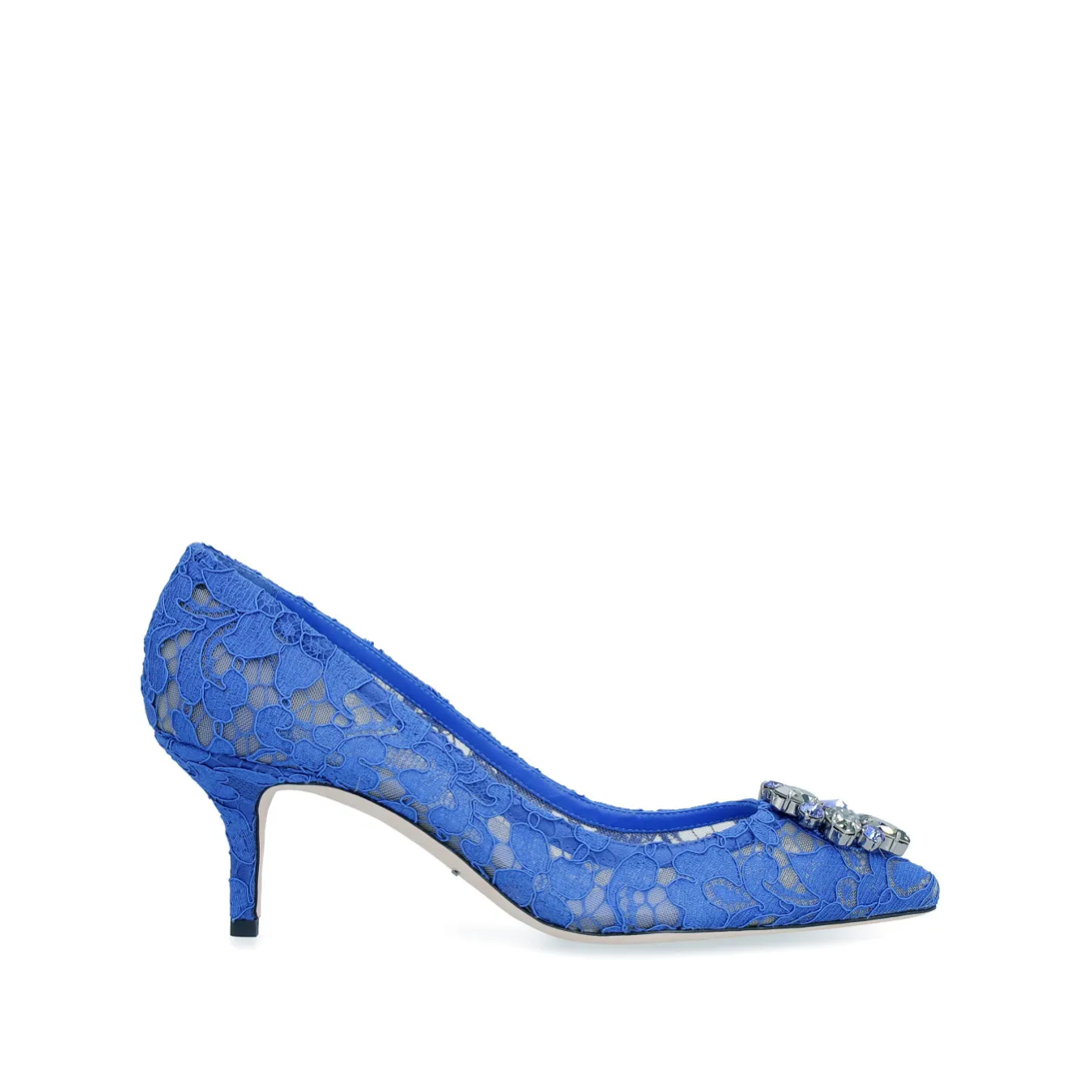 A bright blue lace pump with a pointed toe and a small stiletto heel is displayed against a white background. The shoe is adorned with a sparkling, multi-gem embellishment on the toe. Text overlays the image, reading "From the newest pieces to signature styles, explore Dolce&Gabbana Shoes on FARFETCH".