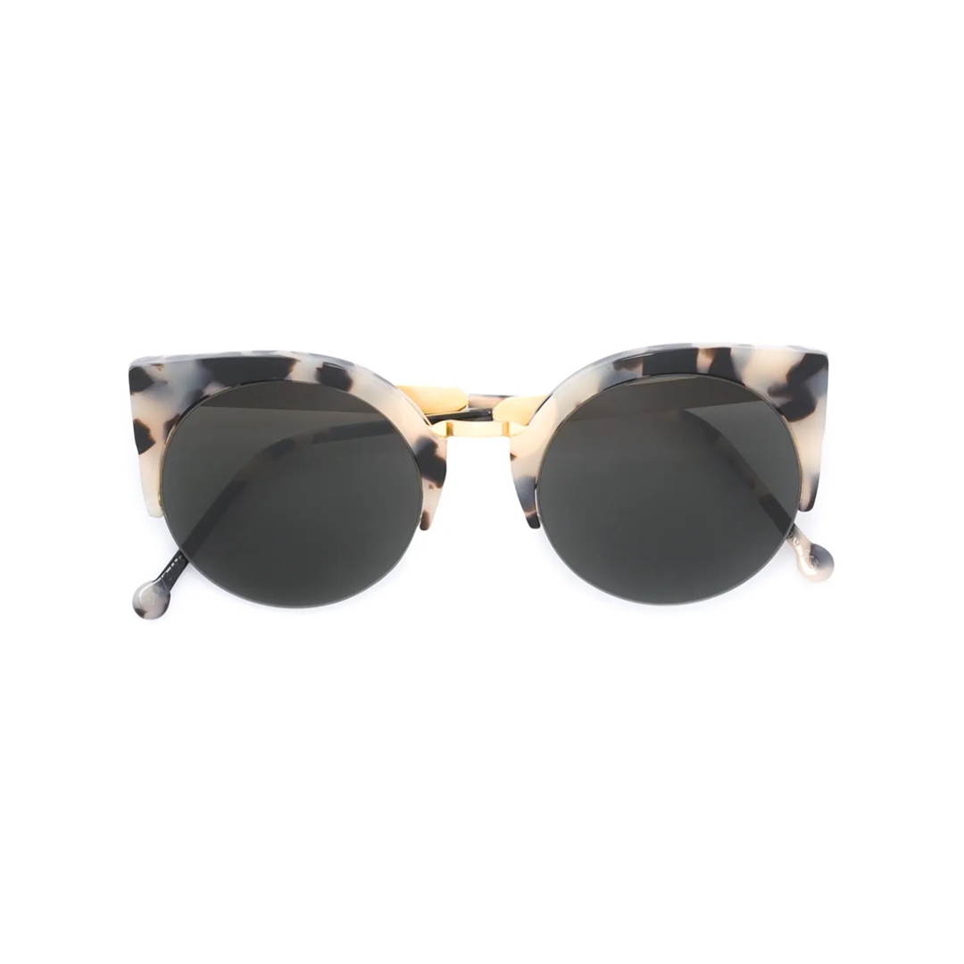 A pair of round, tortoise-shell patterned sunglasses with dark lenses is centered on a white background. The frames have a distinctive cat-eye shape at the top and a subtle gold bridge. The image is a clean product shot, with no additional elements or text visible on the creative itself. The focus is solely on the design and details of the sunglasses.