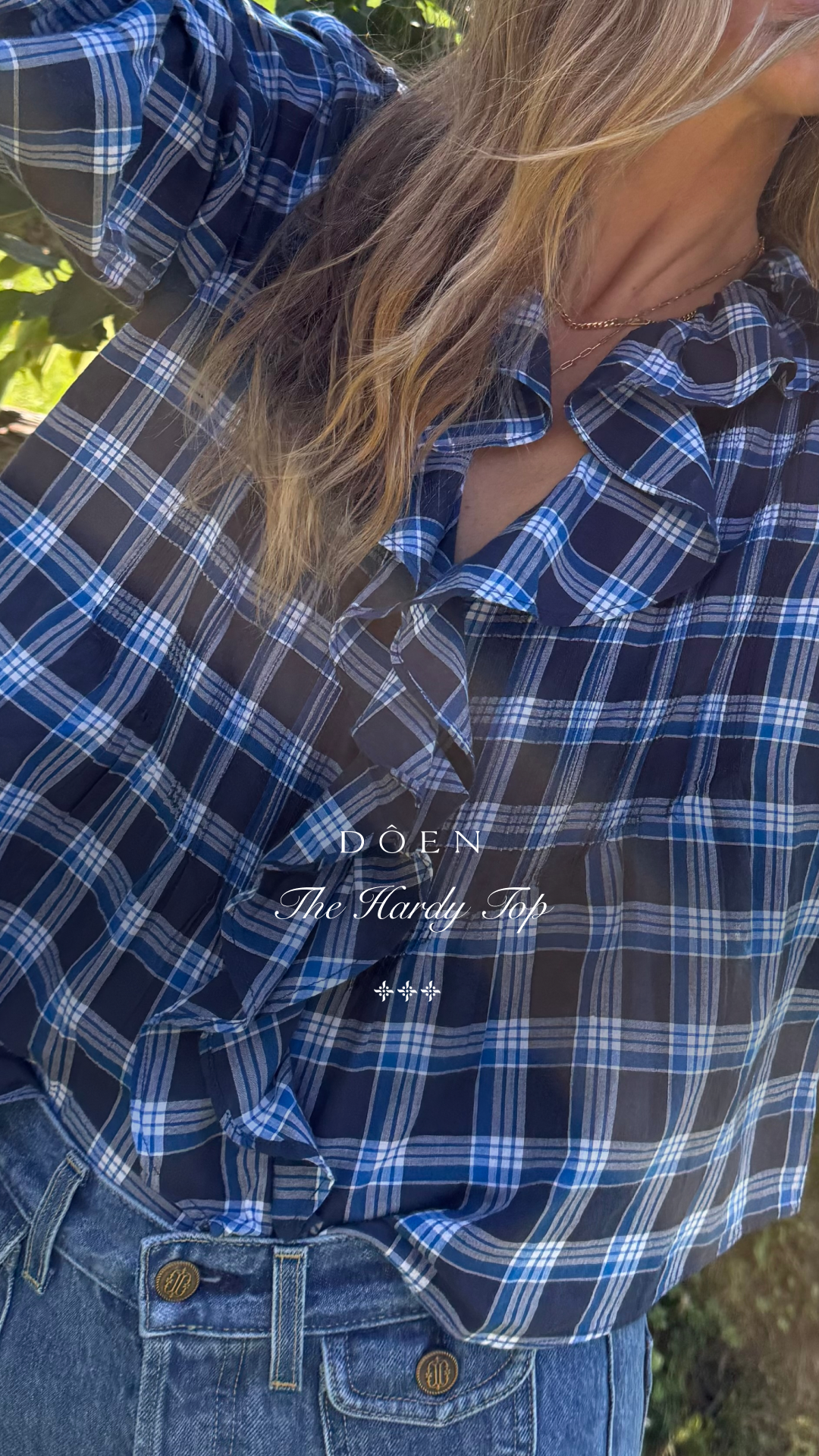 A close-up shot of a woman wearing a blue and white plaid ruffled blouse and denim jeans. The text "DOEN The Hardy Top" is overlaid in the center of the image. The woman has long blonde hair that is partially obscuring her face and shoulder. The background is softly blurred with green foliage and sunlight, suggesting an outdoor setting. The overall impression is a stylish and timeless look.