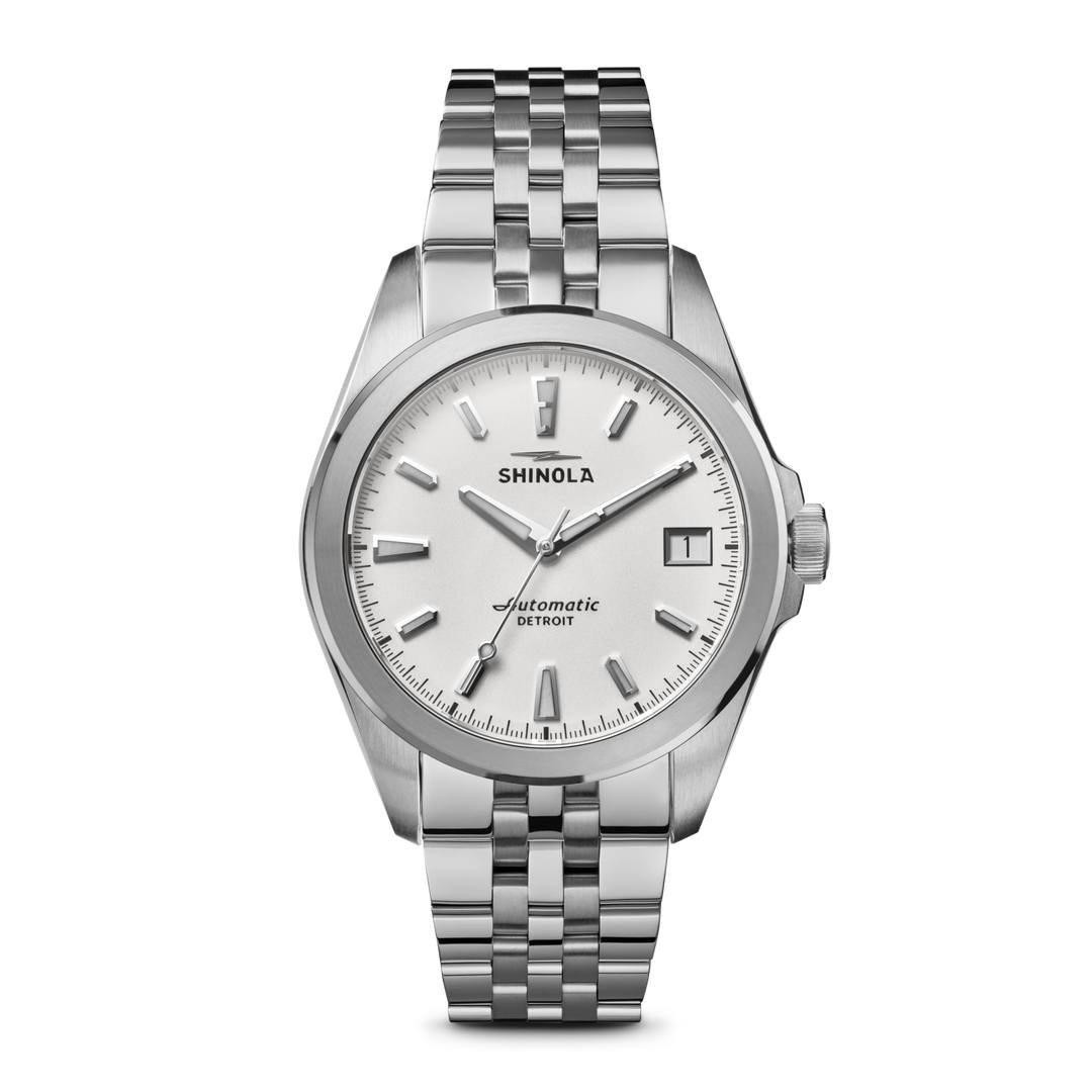 A clean, studio shot of a Shinola automatic watch with a silver dial and a stainless steel band. The watch face displays the brand name 'SHINOLA' and 'Automatic DETROIT'. The text overlay at the top of the image reads 'A Detroit-assembled automatic timepiece inspired by the Great Lakes and built to last.' The bottom text reads 'Discover the Monster collection - made to move with you.'