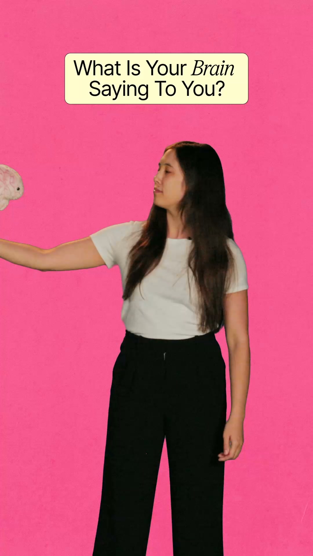 A young woman stands against a bright pink background, holding a small, white, fluffy object that resembles a brain or a stuffed animal. She is looking off to the side, away from the camera. Above her, a yellow rectangular box contains the text "What Is Your Brain Saying To You?" in a stylized font. The overall aesthetic is vibrant and slightly surreal, with the text posing a direct question to the viewer.