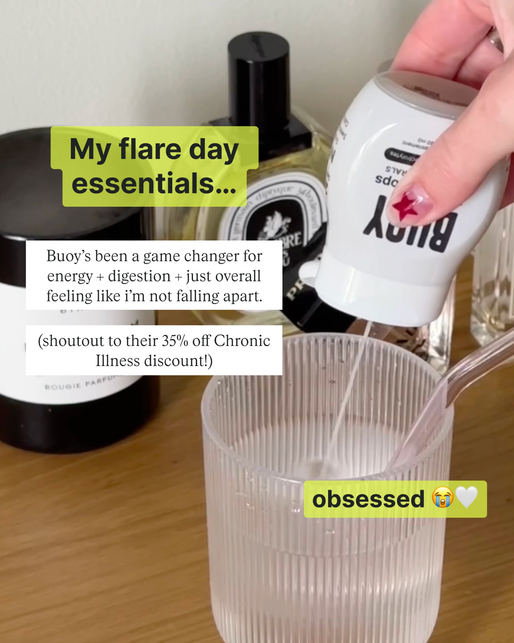 A close-up shot shows a hand pouring liquid from a white bottle labeled "Buoy" into a clear glass filled with water. In the background, several elegant perfume bottles are visible. Text overlays on the image read "My flare day essentials..." and "obsessed ", along with crying and white heart emojis. A separate text box states that Buoy has been a game-changer for energy and digestion, and mentions a 35% off Chronic Illness discount.